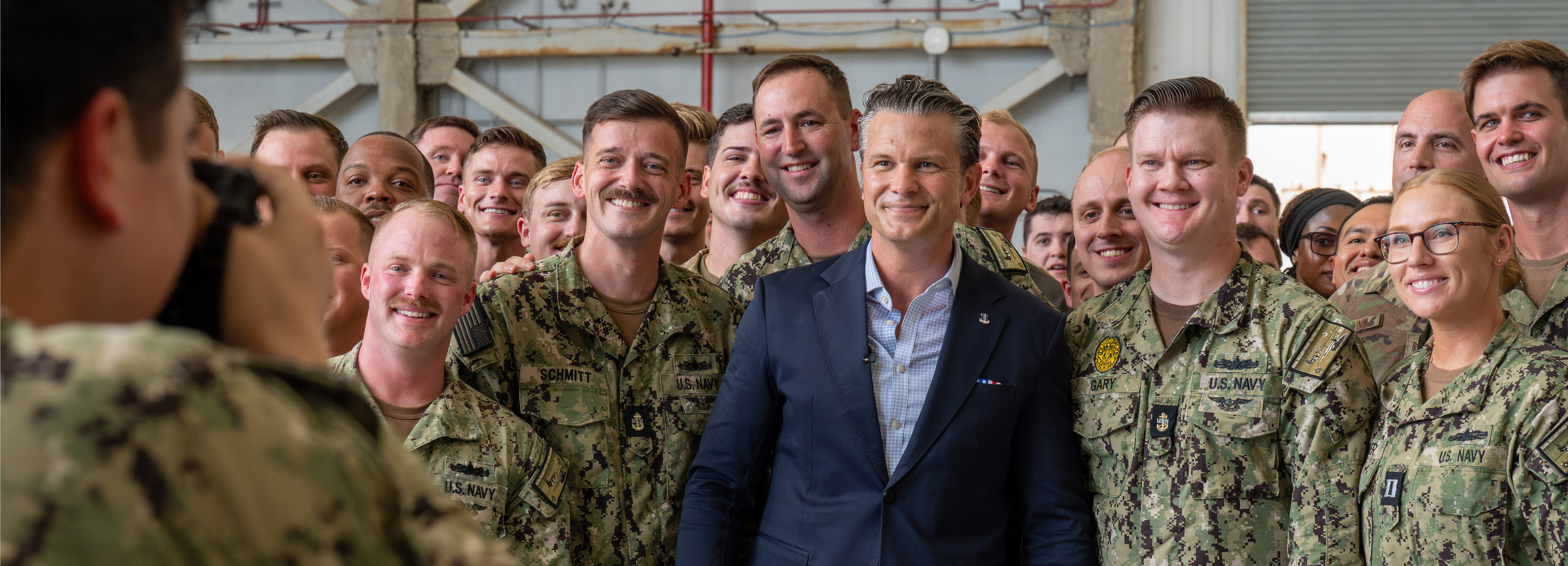 A man poses in the center of a group of service members for a photo.